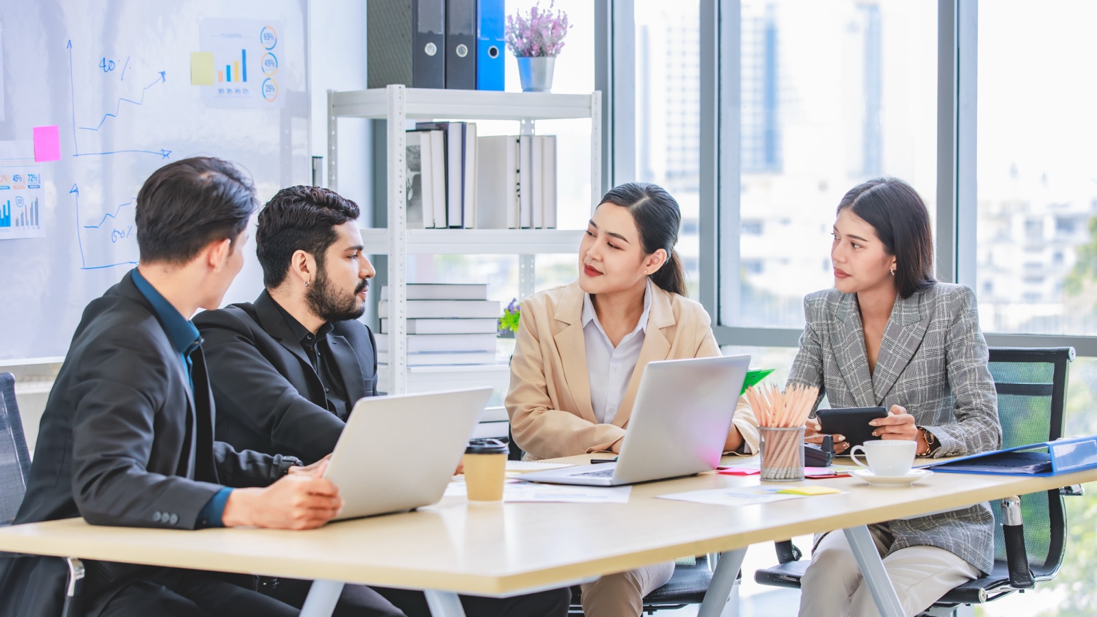 A diverse team of Indian professionals in a meeting, working on laptops around a table