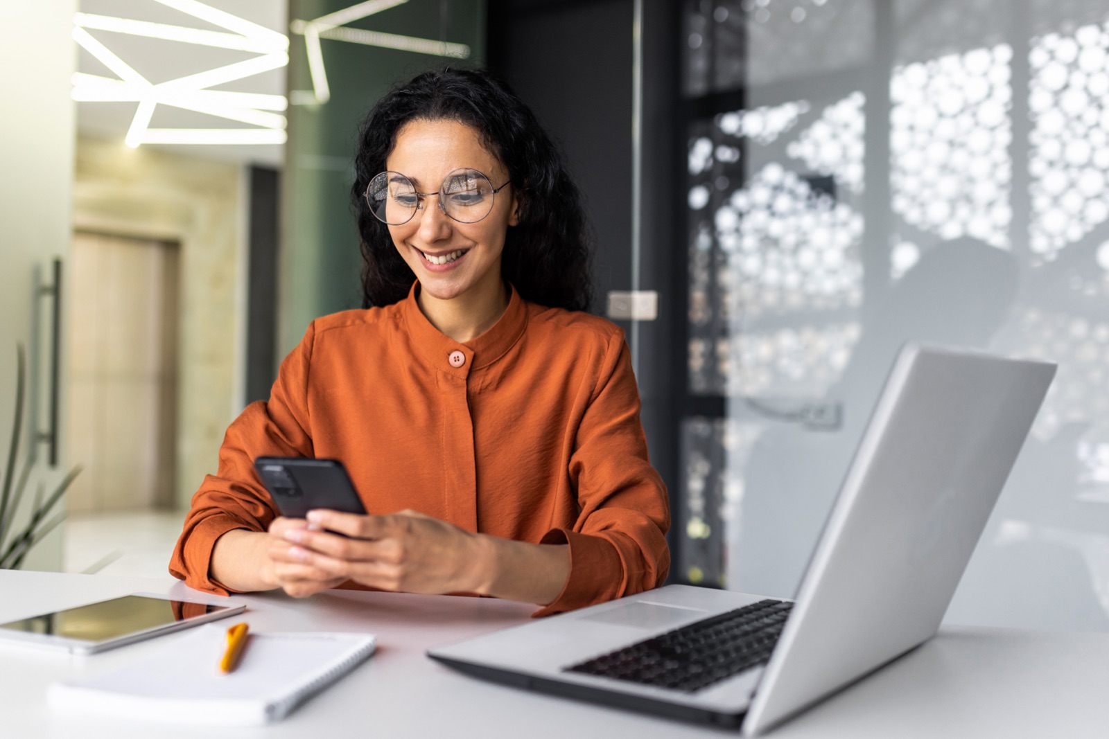 A smiling employee checking the HRMS app on her phone at her office desk